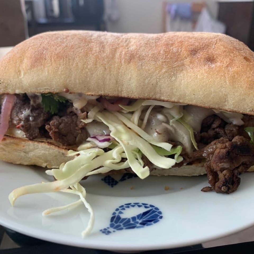 A Café Etoile sandwich with meat, shredded cabbage, and pickled onions on a white plate.