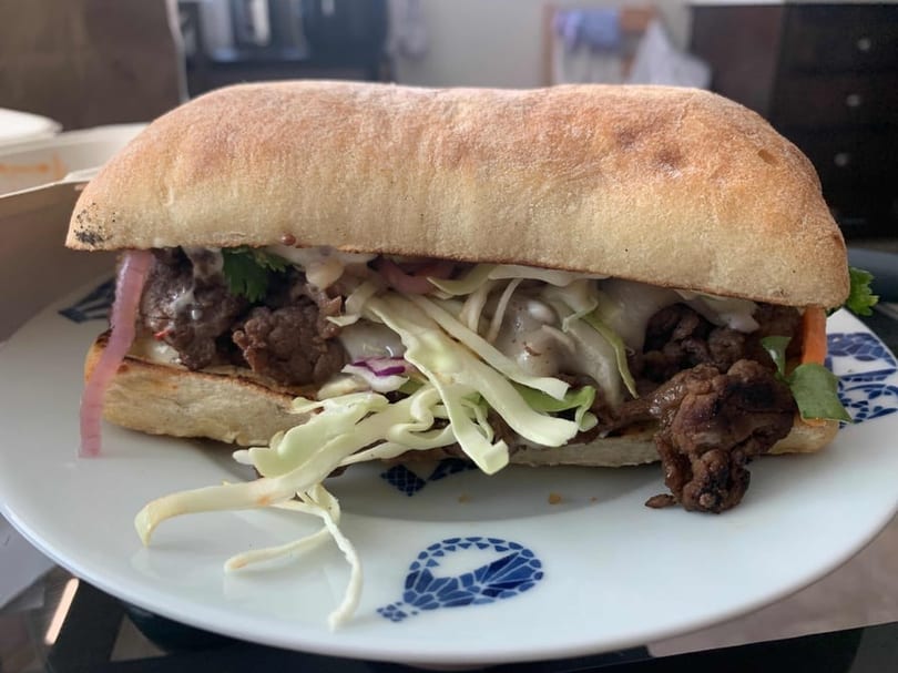 A Café Etoile sandwich with meat, shredded cabbage, and pickled onions on a white plate.