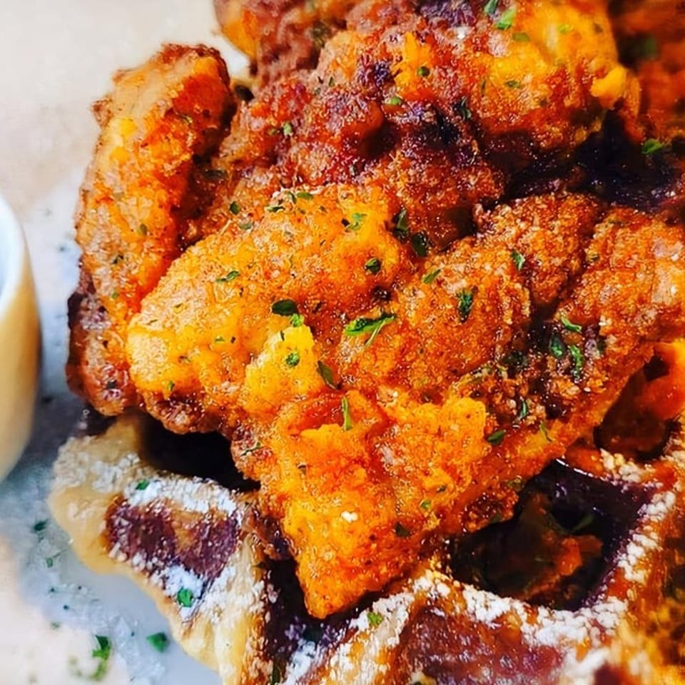 Crispy fried chicken pieces on a waffle dusted with powdered sugar, with a side of syrup.