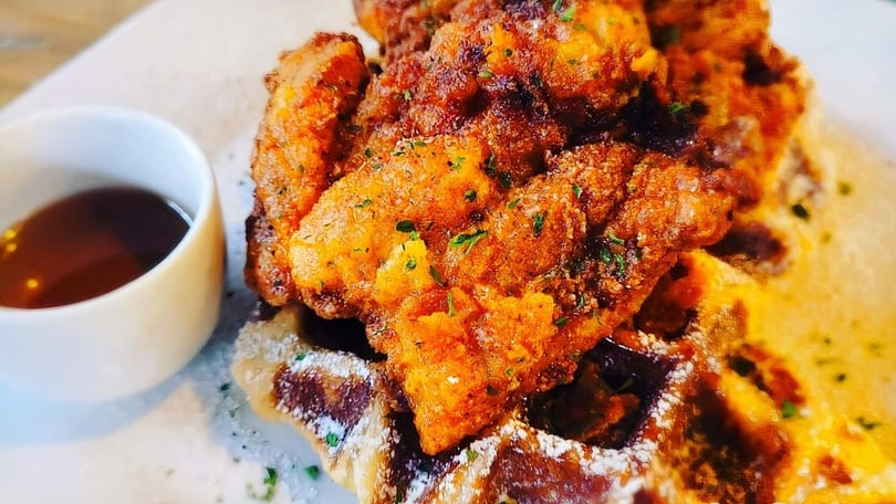 Crispy fried chicken pieces on a waffle dusted with powdered sugar, with a side of syrup.