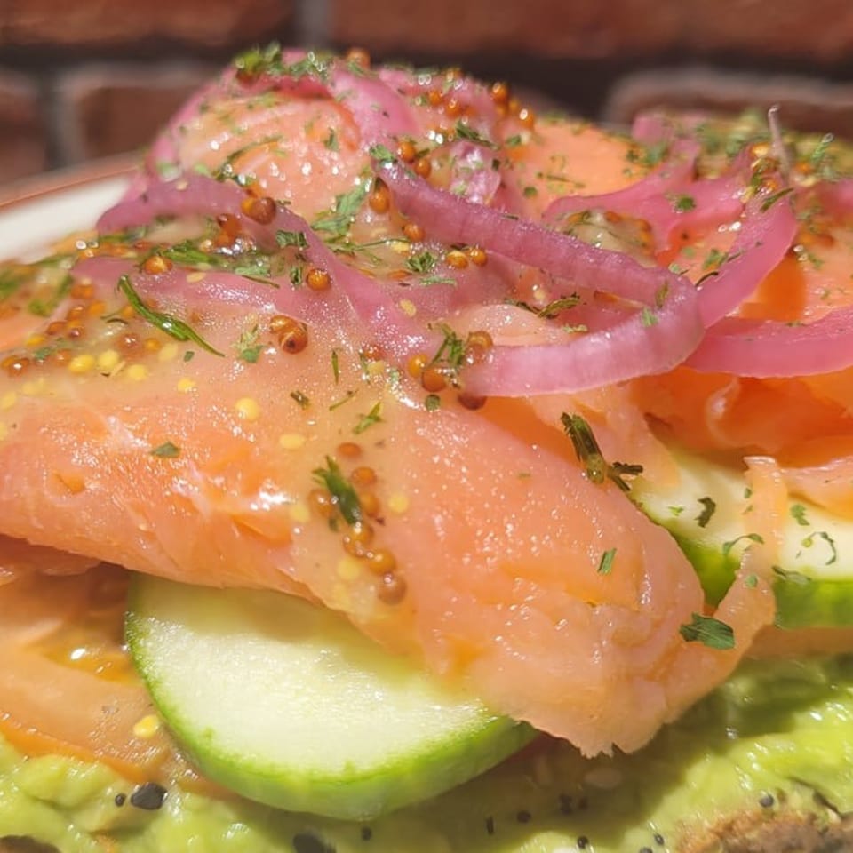 Close-up of Café Etoile's salmon avocado toast with pickled onions, tomatoes, and cucumbers.