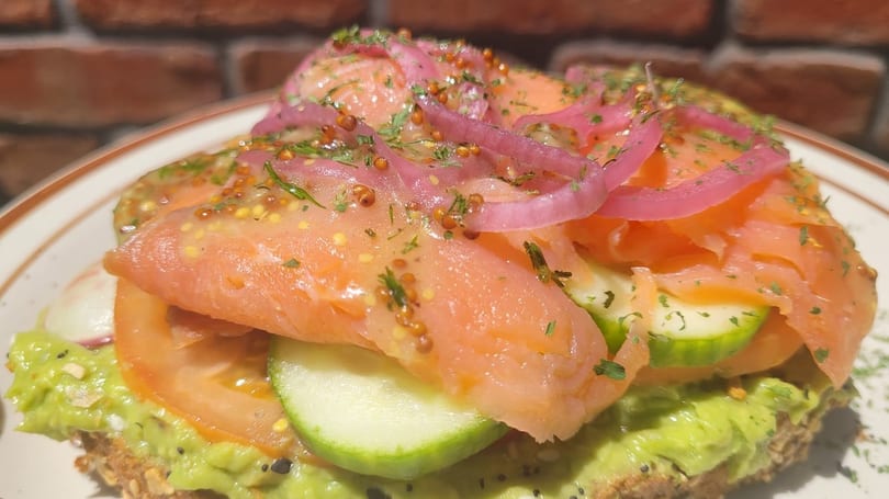 Close-up of Café Etoile's salmon avocado toast with pickled onions, tomatoes, and cucumbers.
