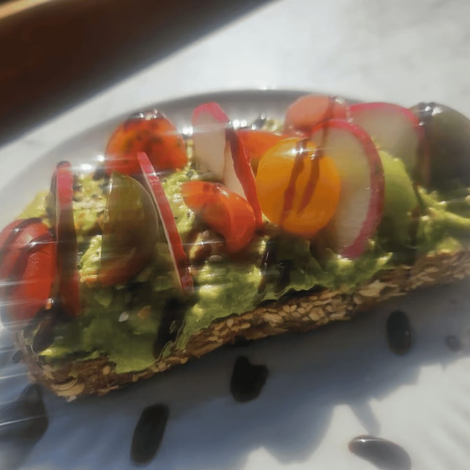 Avocado toast topped with colorful cherry tomatoes, sliced radishes, and a balsamic glaze.