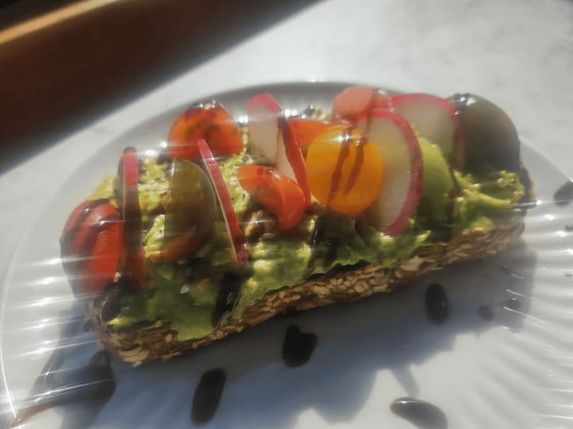 Avocado toast topped with colorful cherry tomatoes, sliced radishes, and a balsamic glaze.